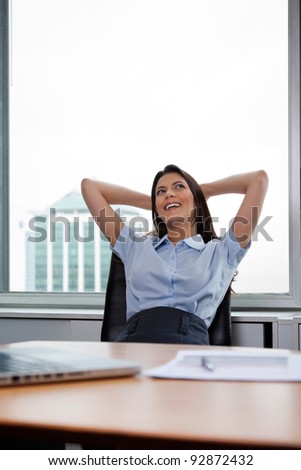 Pretty businesswoman sitting on office chair and relaxing with hands behind head