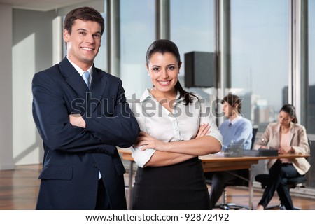 Portrait of business executives with arms crossed with colleagues working in background