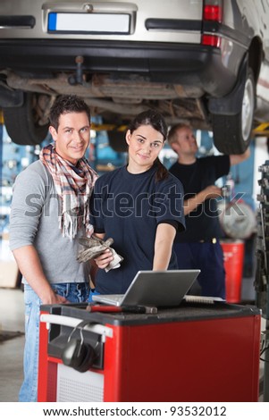Portrait of female worker using laptop while standing next to the client in garage with person in the background