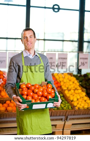 A friendly grocery store owner with a box of ripe tomatoes
