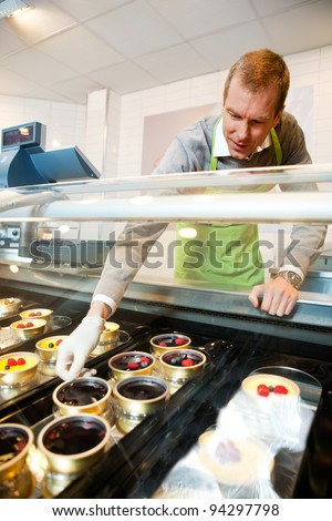 A man selling gourmet deserts from behind a glass counter