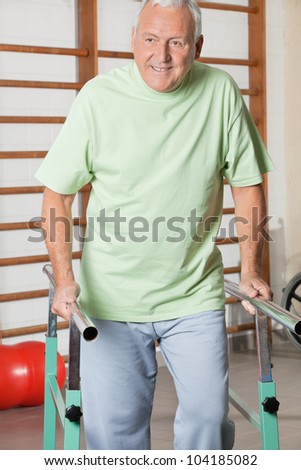 Happy senior man walking with the help of support bars at hospital gym