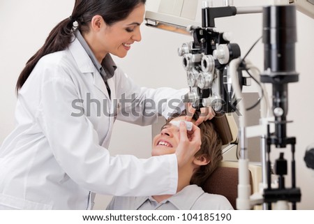 Smiling young optometrist putting eye drops in eyes of patient for clear vision
