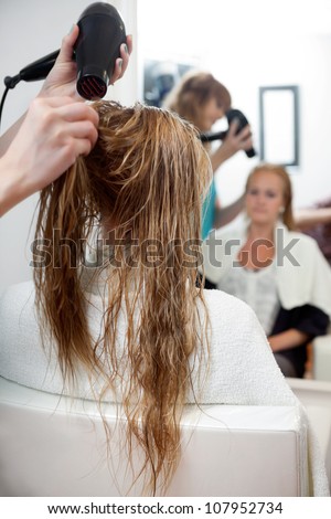 Hairdressers hands drying long blond hair with blow dryer at parlor