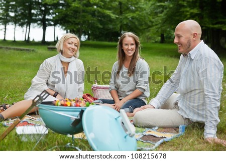 Happy Caucasian friends on picnic with portable barbeque in forest park