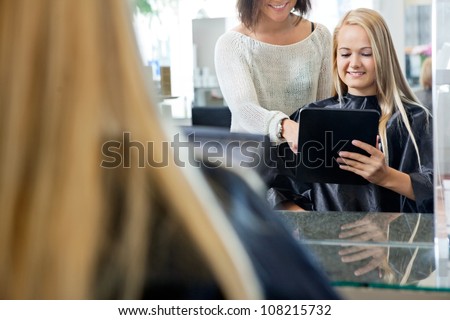Mirror reflection of female customer holding digital tablet with hairdresser standing behind her