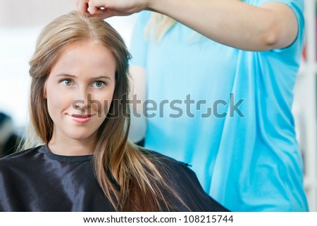 Young woman smiling while hairdresser getting her ready for haircut at parlor
