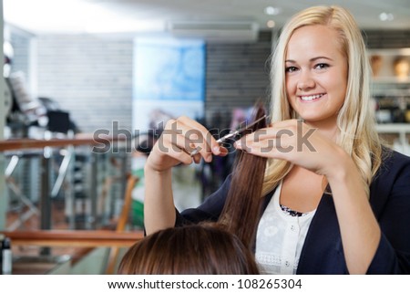 Portrait of happy young female beautician giving a haircut to female at parlor