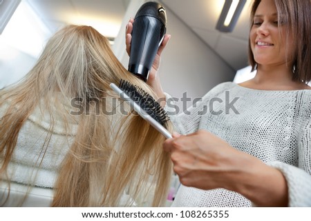Low angle view of hairdresser drying long blond hair with blow dryer and brush