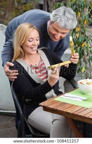 Happy middle aged woman looking at present from man while sitting at table