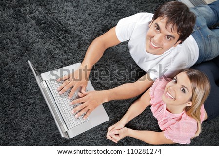 High angle view of young couple lying on rug with laptop