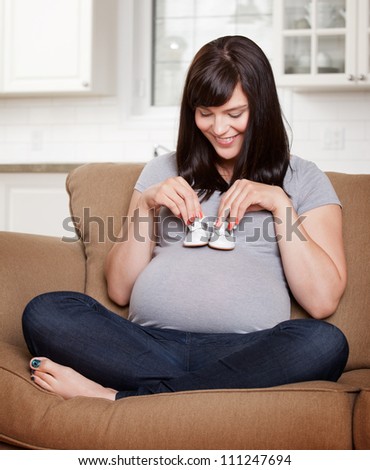 Expecting young mother holding baby shoes on belly