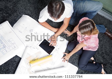 High angle view of couple sitting on rug with blueprints and digital tablet