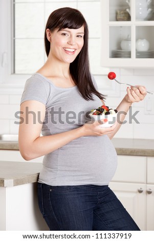 Happy pregnant woman eating a healthy snack of granola and fruit