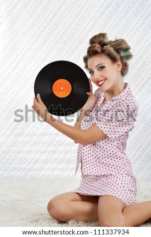 Portrait of young woman with hair curlers holding an old vinyl record while sitting on rug