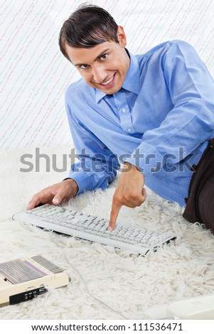Portrait of geek businessman pressing keyboard keys while lying down on rug with an old fashioned cassette player