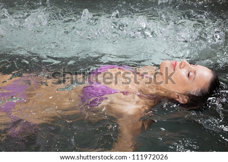 An attractive young woman floating on her back in a Jacuzzi at health spa