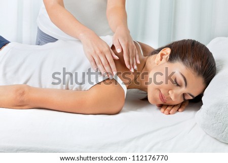 Young woman relaxing with eyes closed as she is receiving back massage by female masseuse