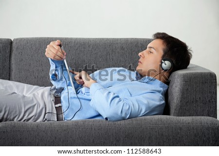 Relaxed young man in formal wear browsing internet while listening to music on digital tablet
