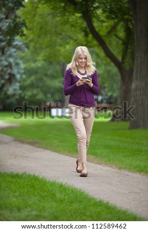 Full length of a young woman using smart phone as she walks in park