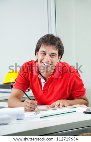 Portrait of young male architect drafting blueprint while sitting at desk