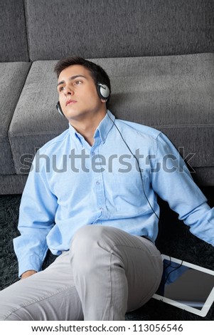 Relaxed young man in formal wear looking away while listening music on digital tablet