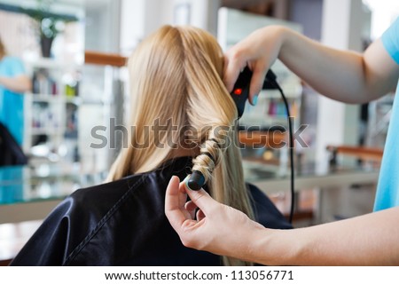 Close up of stylist\'s hand using curling iron for hair curls