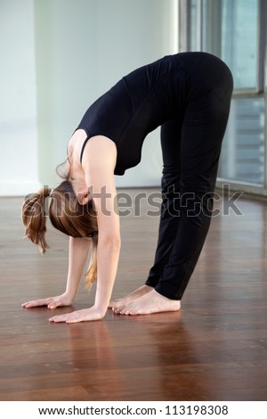 Full length of a young woman doing Standing Forward Bend in gym