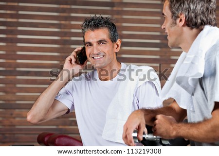 Portrait of happy mature man on call while friend looking at him in health club