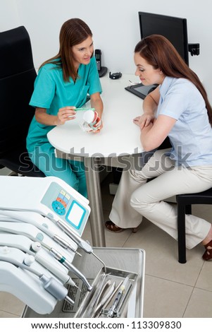 Female dentist using teeth model while explaining dental procedure to patient at desk
