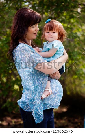 Portrait of a pregnant mother in third trimester together with daughter in park