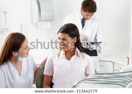 Nurse communicating with female patient while dentist using digital tablet in the background