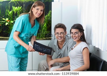 Portrait of a female dentist showing dental X-ray to young couple in clinic