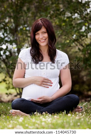 Portrait of an attractive healthy pregnant woman in third trimester sitting in park