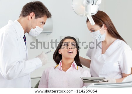 Young male dentist looking at nurse comforting patient in clinic