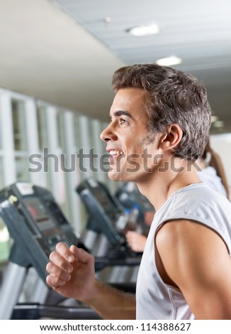 Side view of happy young man and woman running on treadmill in health club