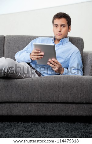 Portrait of young man in formal wear holding digital tablet while sitting on sofa