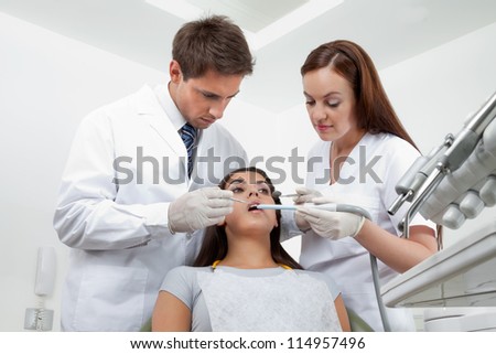 Young male dentist and nurse examining patient\'s teeth in clinic
