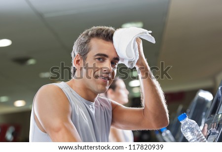 Portrait of young man wiping sweat with towel at health club
