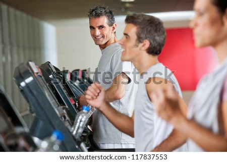 Portrait of happy mature man running on treadmill in fitness club