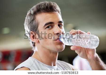 Portrait of young man drinking water from bottle at health club