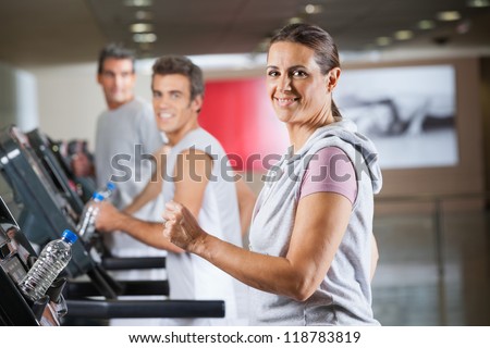 Portrait of happy mature woman and men running on treadmill in fitness center