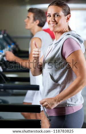 Side view of happy mature woman and man running on treadmill in health club