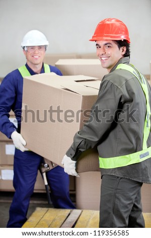 Portrait of two foremen lifting cardboard box in warehouse