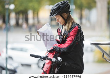 Young female cyclist in protective gear putting package in courier bag on street