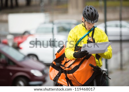 Young male cyclist in protective gear with package and courier bag on street