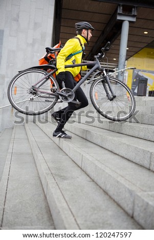 Courier delivery man in protective gear with bicycle and backpack walking up steps