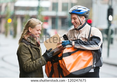 Smiling young woman receiving a package from courier delivery man with backpack
