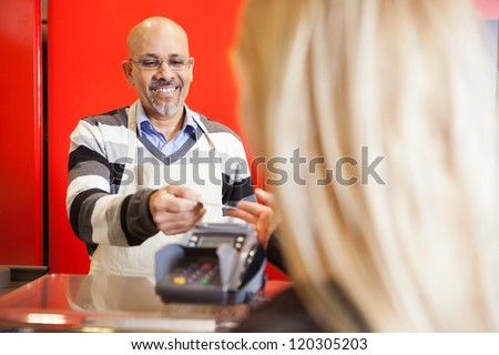 Mature man accepting credit card from young woman for payment of purchases
