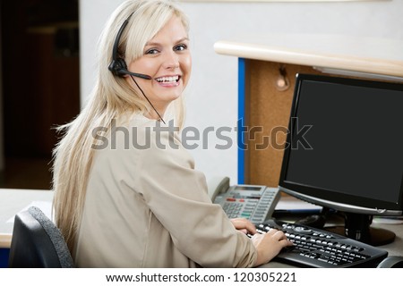 Portrait of cheerful young woman using computer at reception desk